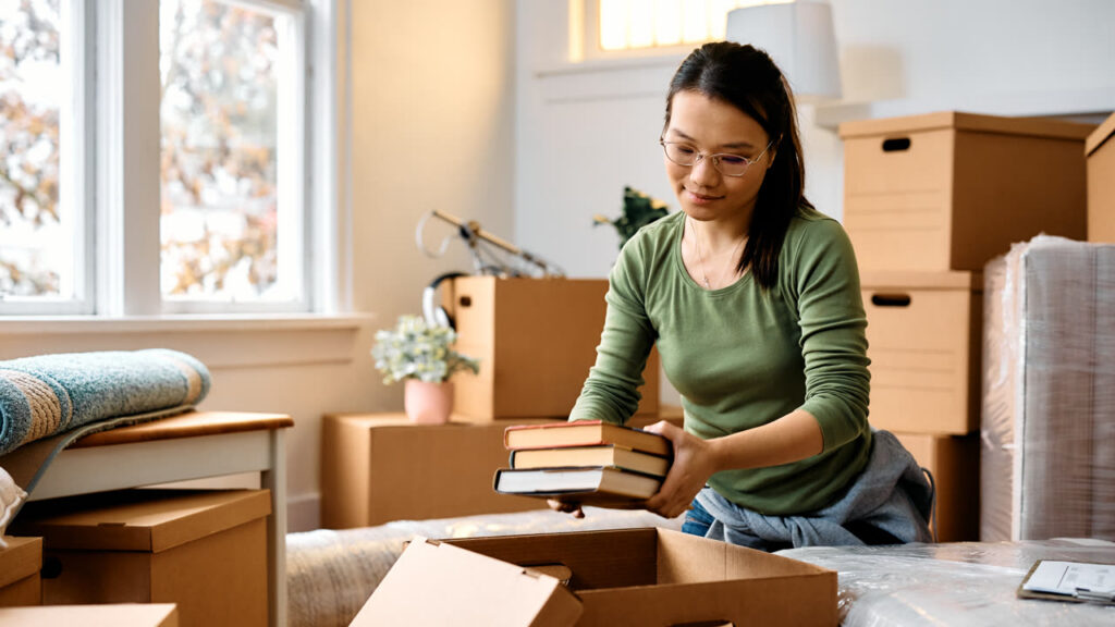 A woman packing books into a cardboard box while moving to a new home