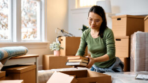 A woman packing books into a cardboard box while moving to a new home