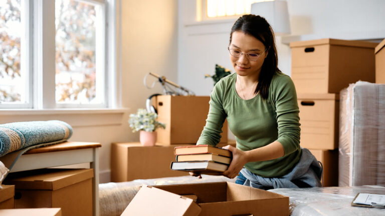 A woman packing books into a cardboard box while moving to a new home