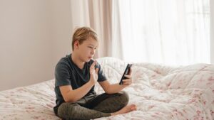 A teenage boy sitting cross-legged on his bed looking at a smartphone