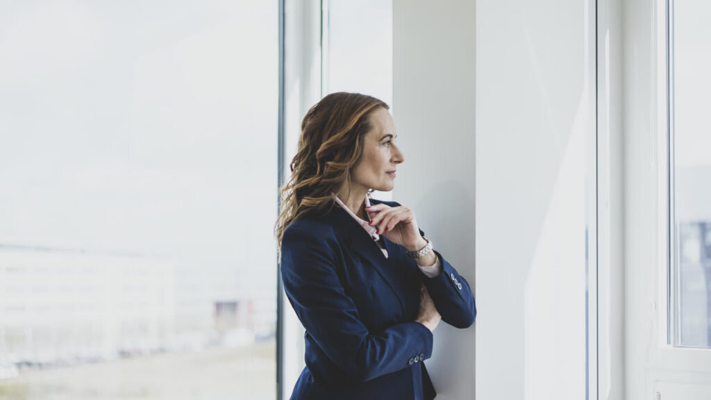 A woman standing by an office window, pausing to look out during the workday