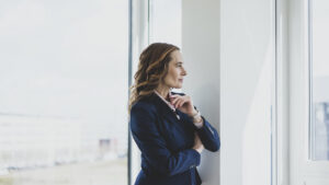 A woman standing by an office window, pausing to look out during the workday