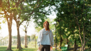 A woman walking along a tree-lined park path in morning sunlight