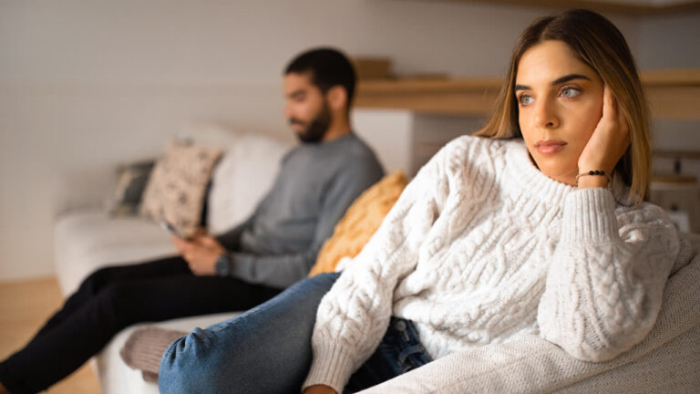 A couple sitting apart on the couch, turned away from each other after a disagreement